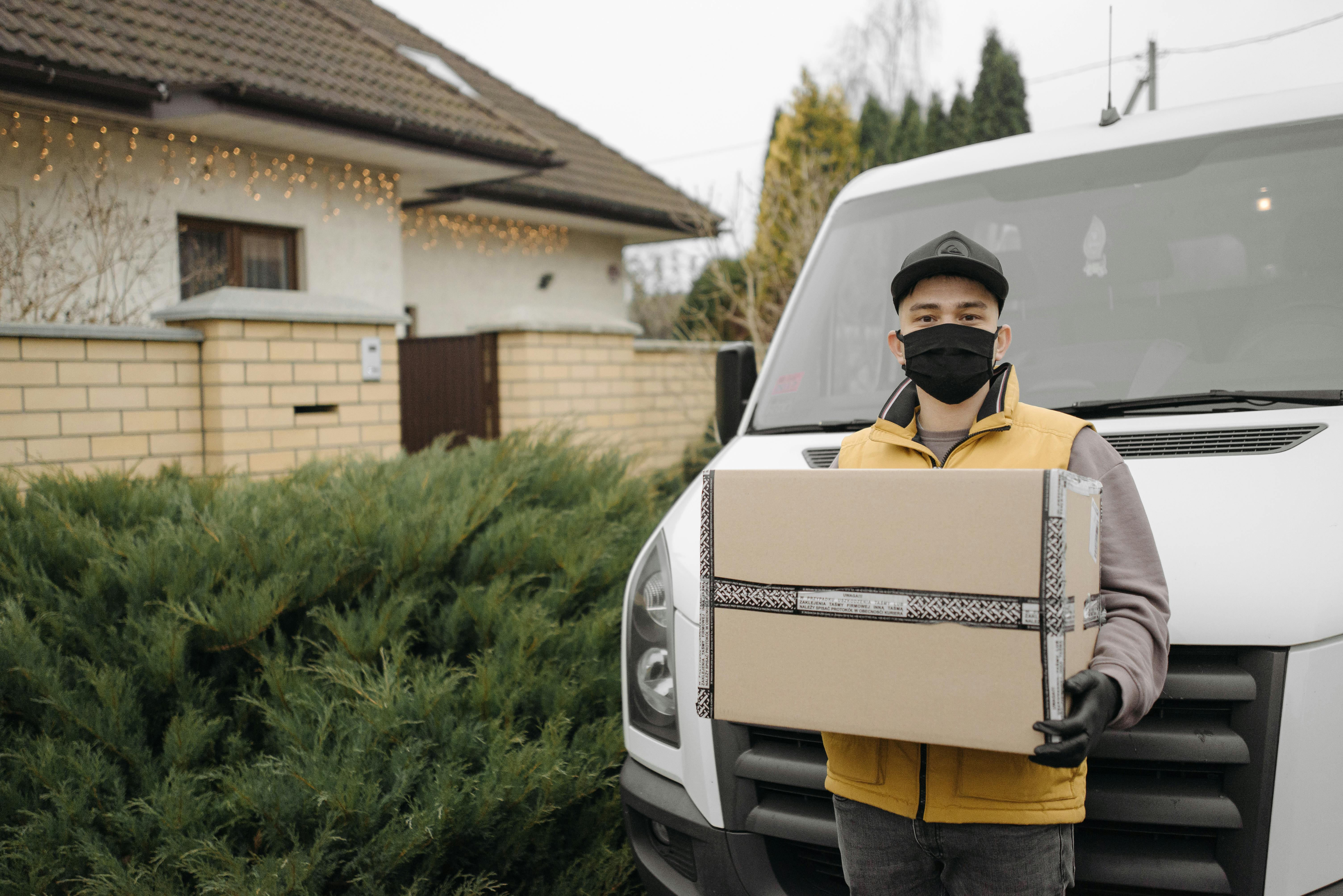[A pharmacy delivery driver handing over a sealed medicines box to a care home nurse at a residential facility entrance]